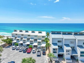 A beachfront hotel with multiple-story buildings, a parking lot with several cars, and a view of the ocean. - Blue Mountain Beach Villas 5B (Santa Rosa Beach)