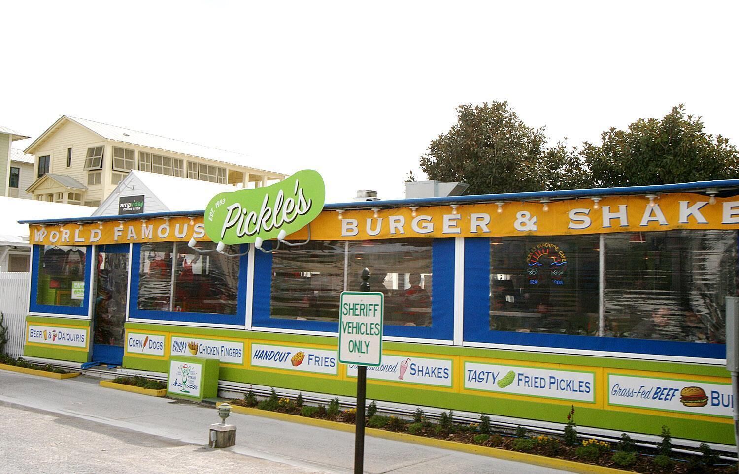 Un puesto de comida a la carretera con letreros que dicen 'Encurtidos', 'Hamburguesas y Batidos' y 'Famoso en todo el mundo'.