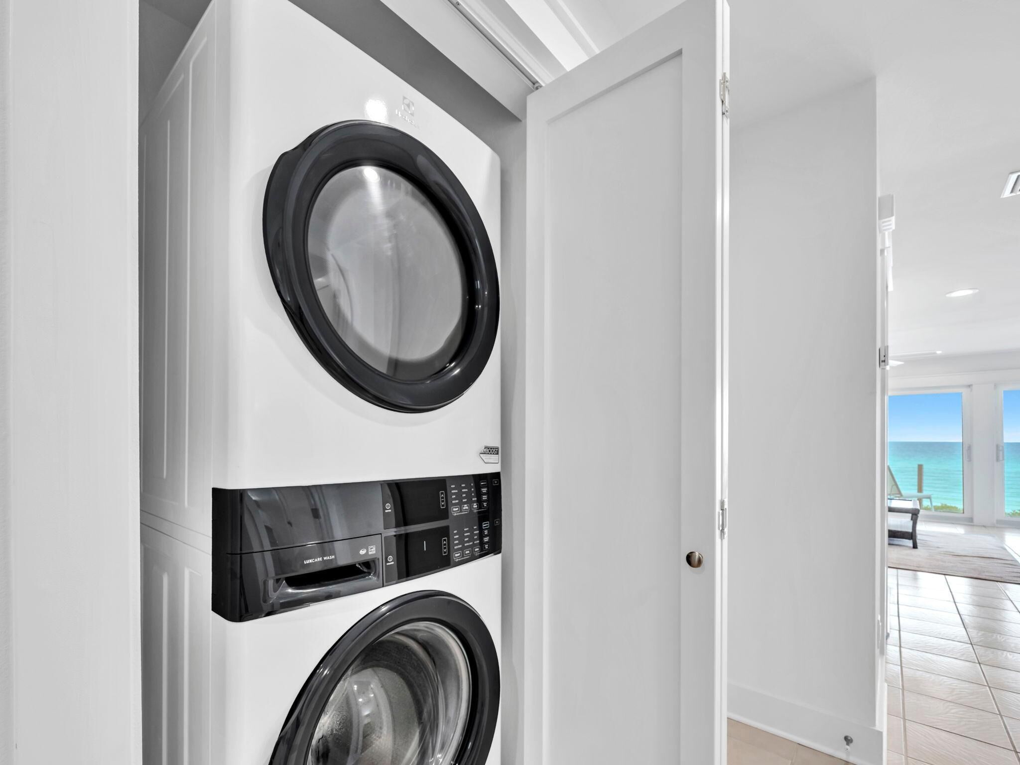 A laundry room with two front-loading washing machines, a control panel, and a door leading to a room with a view of the ocean.