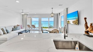 Eine moderne Küche mit einer großen Kochinsel, ein Essbereich mit Meerblick und ein Wohnbereich mit Sofa und Sesseln.