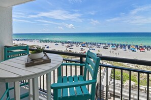 A balcony with a table and chairs overlooking a beach with umbrellas and people. - Sundestin 510 (Destin)