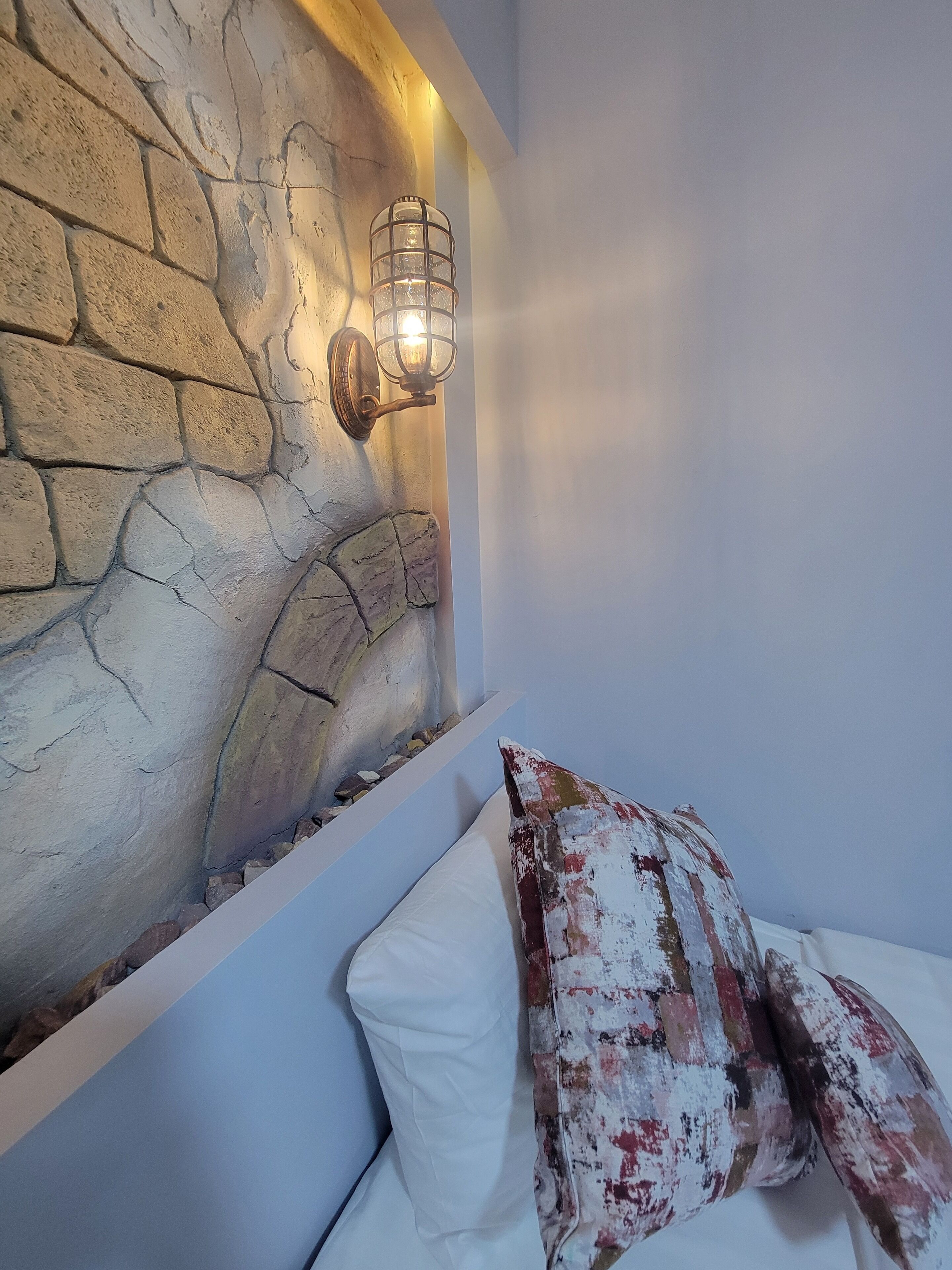 Ein Schlafzimmer mit einer Steinwand und einem Bett mit weißen und bunten Kissen.