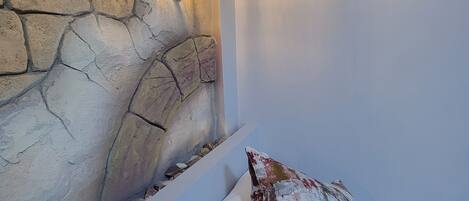 A bedroom with a stone wall and a bed with white and multicolored pillows.