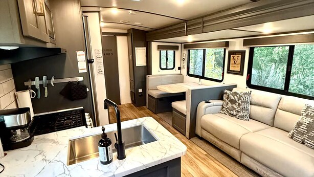 A compact RV interior with a kitchen area, a dining space, and a seating area with a sofa and windows. - Camper in Zephyrhills with Wi-Fi (Zephyrhills)