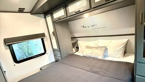 A compact, modern RV bedroom with a bed, a small window, and a headboard with a geometric pattern. - Camper in Zephyrhills with Wi-Fi (Zephyrhills)