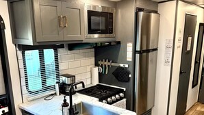 A compact kitchen with a built-in microwave, stove, and refrigerator, featuring a marble countertop and dark cabinetry. - Camper in Zephyrhills with Wi-Fi (Zephyrhills)