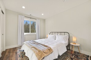 Une chambre à coucher avec un lit, une table de chevet avec une lampe, une fenêtre avec des rideaux et un tapis à motifs.