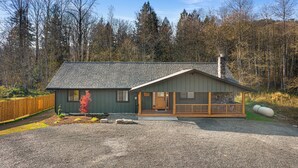 A small cabin with a porch, a stone chimney, and a wooden fence in the background. - Book Your Mt. Baker Après Ski Stay (Deming)