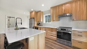 A modern kitchen with wooden cabinets, a stainless steel refrigerator, an oven, and a large island with stools. - Book Your Mt. Baker Après Ski Stay (Deming)
