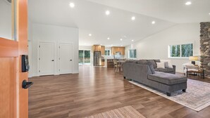 A spacious living area with a gray sectional sofa, a dining table, and a kitchen in the background. - Book Your Mt. Baker Après Ski Stay (Deming)