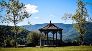 Un kiosque se dresse dans un champ verdoyant, avec des montagnes en toile de fond.