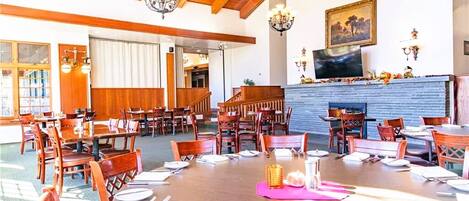 A dining area with wooden tables and chairs, a fireplace, and a television on the wall.
