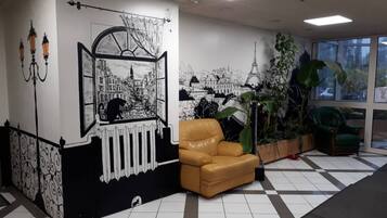 A lobby with a checkered floor, a brown leather chair, a large potted plant, and a mural depicting a cityscape.