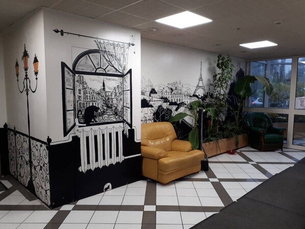 A lobby with a checkered floor, a brown leather chair, a large potted plant, and a mural depicting a cityscape. - Appart Hotel (Champagne-sur-Oise)
