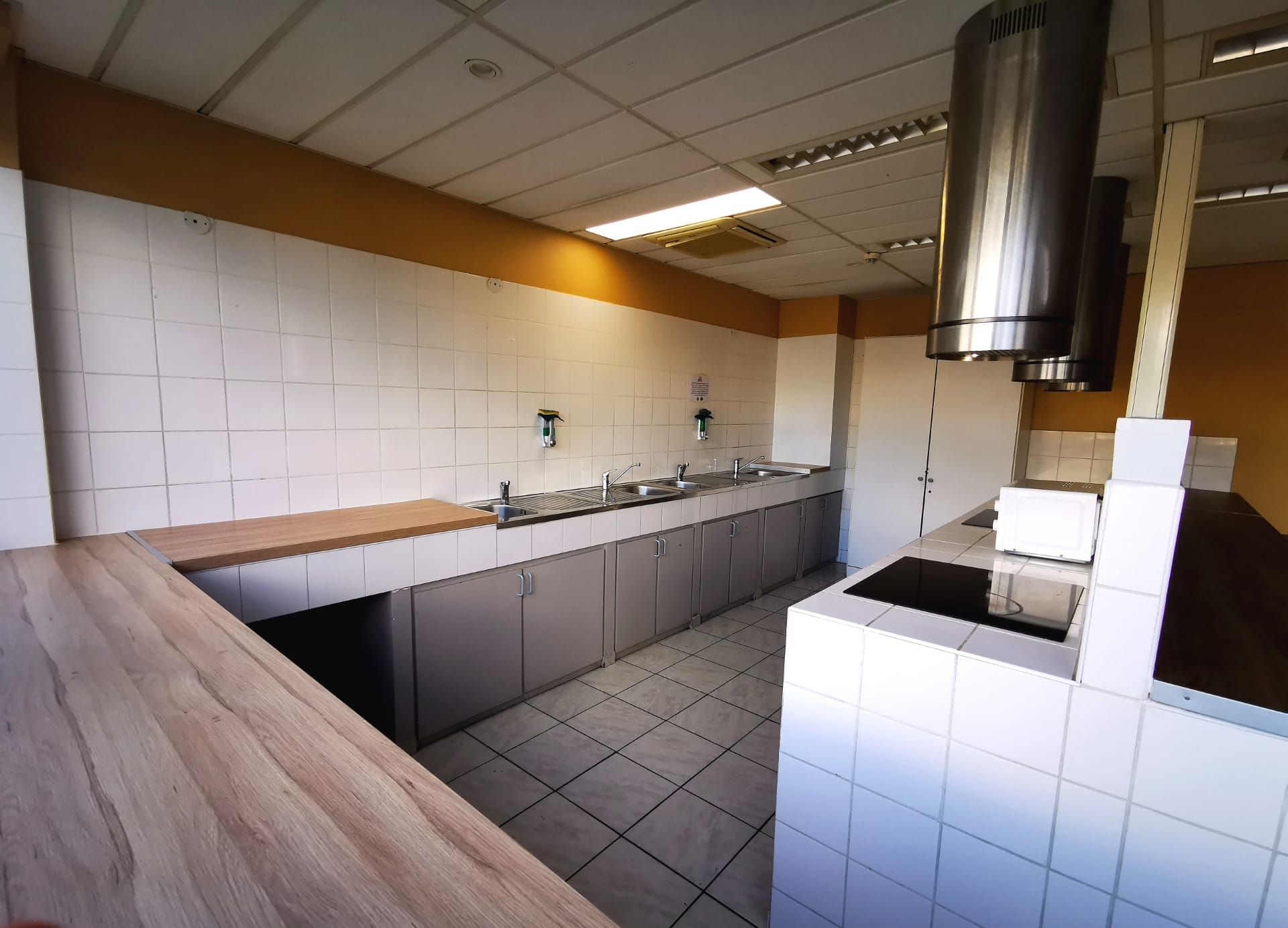 A modern kitchen with white tiles, grey cabinets, and a wooden countertop.
