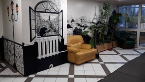 Eine Lobby mit Schachbrettmuster-Boden, einem braunen Ledersessel, einer großen Topfpflanze und einem Wandbild, das eine Stadtansicht zeigt.