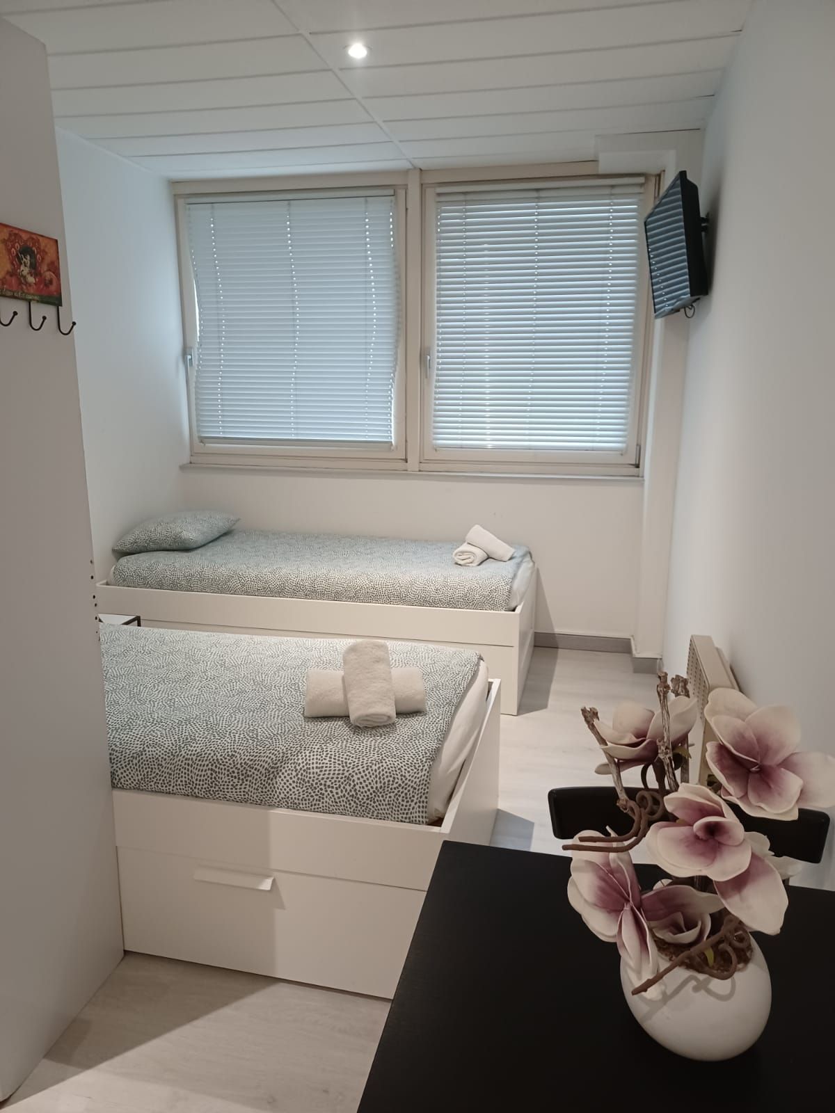 Une chambre avec deux lits, un bureau et un vase de fleurs.