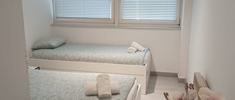 A bedroom with two beds, a desk, and a vase with flowers.