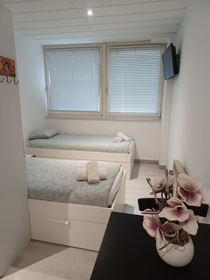 A bedroom with two beds, a desk, and a vase with flowers. - Appart Hotel (Champagne-sur-Oise)