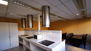 A modern kitchen with a central island, stainless steel range hood, and a dining area with a table and chairs. - Appart Hotel (Champagne-sur-Oise)
