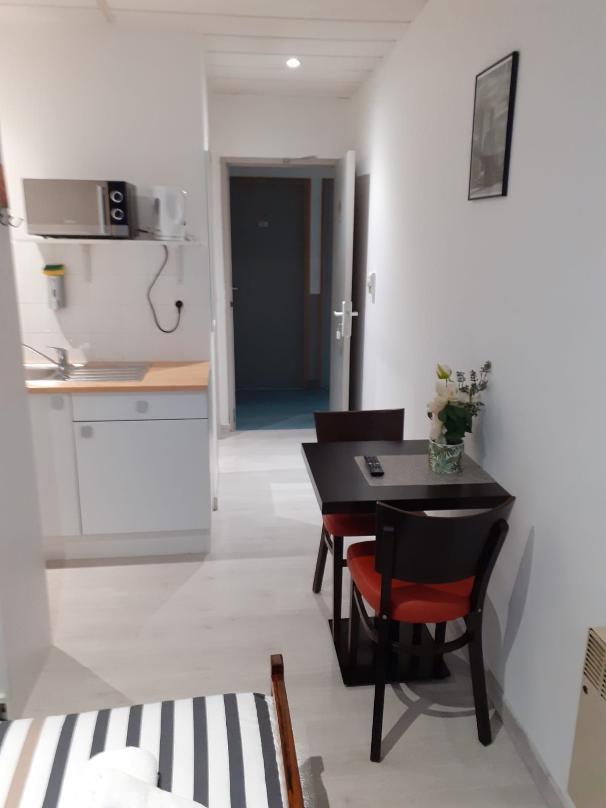 Un couloir étroit mène à un coin repas comprenant une table et des chaises, un four à micro-ondes et un petit espace cuisine.