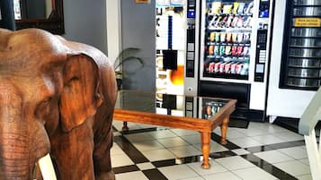 A reception area with a checkered floor, a wooden bench, a large elephant sculpture, vending machines, and a staircase.