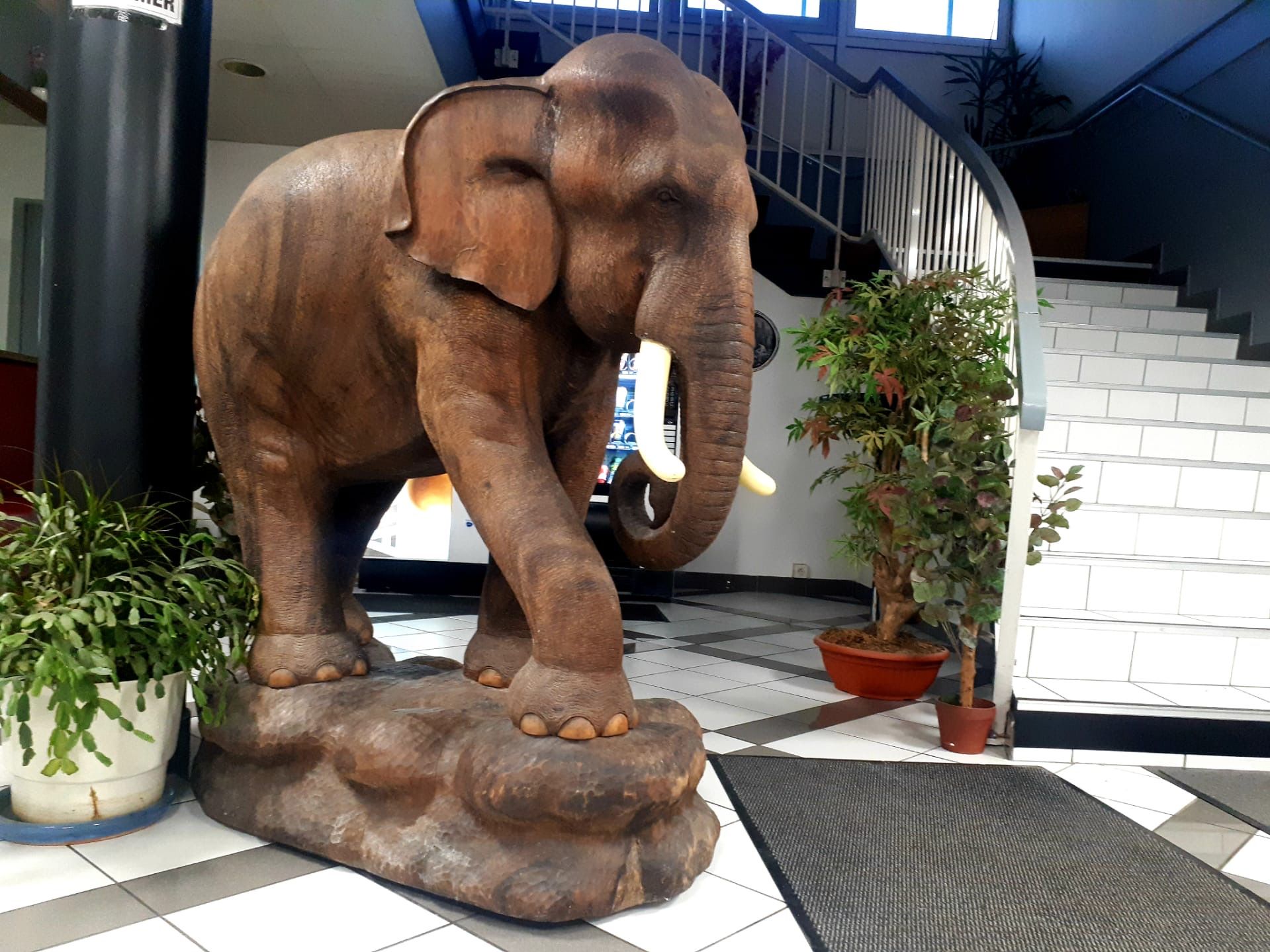 A large elephant statue on a platform with potted plants around it.