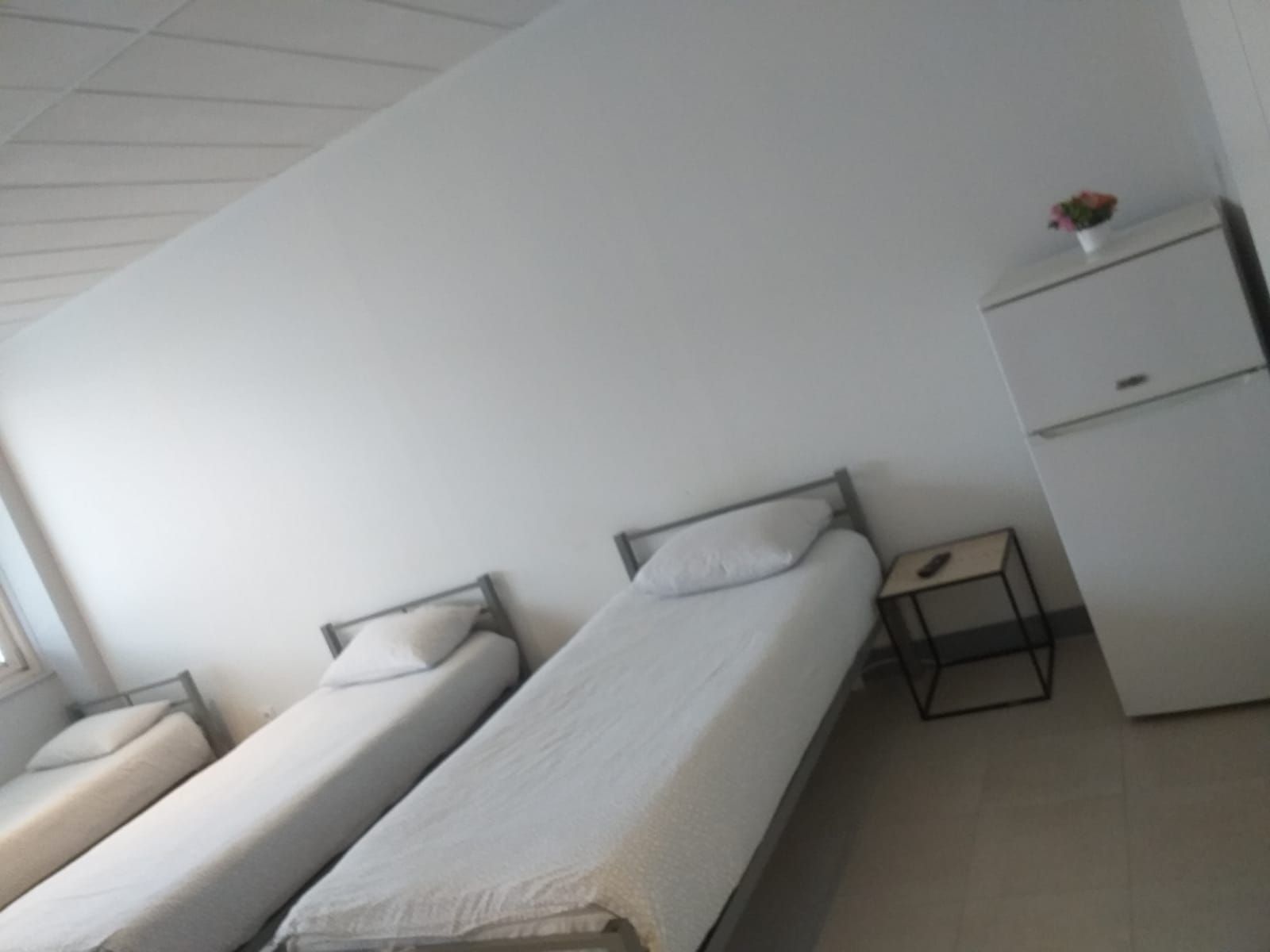 A dormitory room with two single beds, a small desk, and a wardrobe.