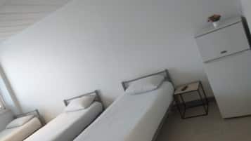 A dormitory room with two single beds, a small desk, and a wardrobe.