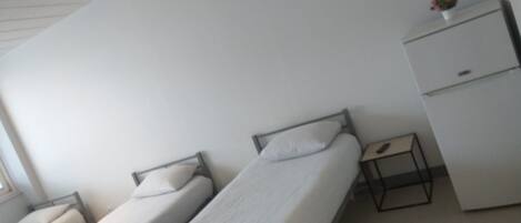 A dormitory room with two single beds, a small desk, and a wardrobe.
