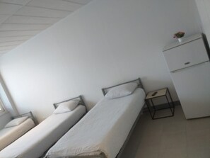 Habitación tipo dormitorio con dos camas individuales, un escritorio pequeño y un armario.