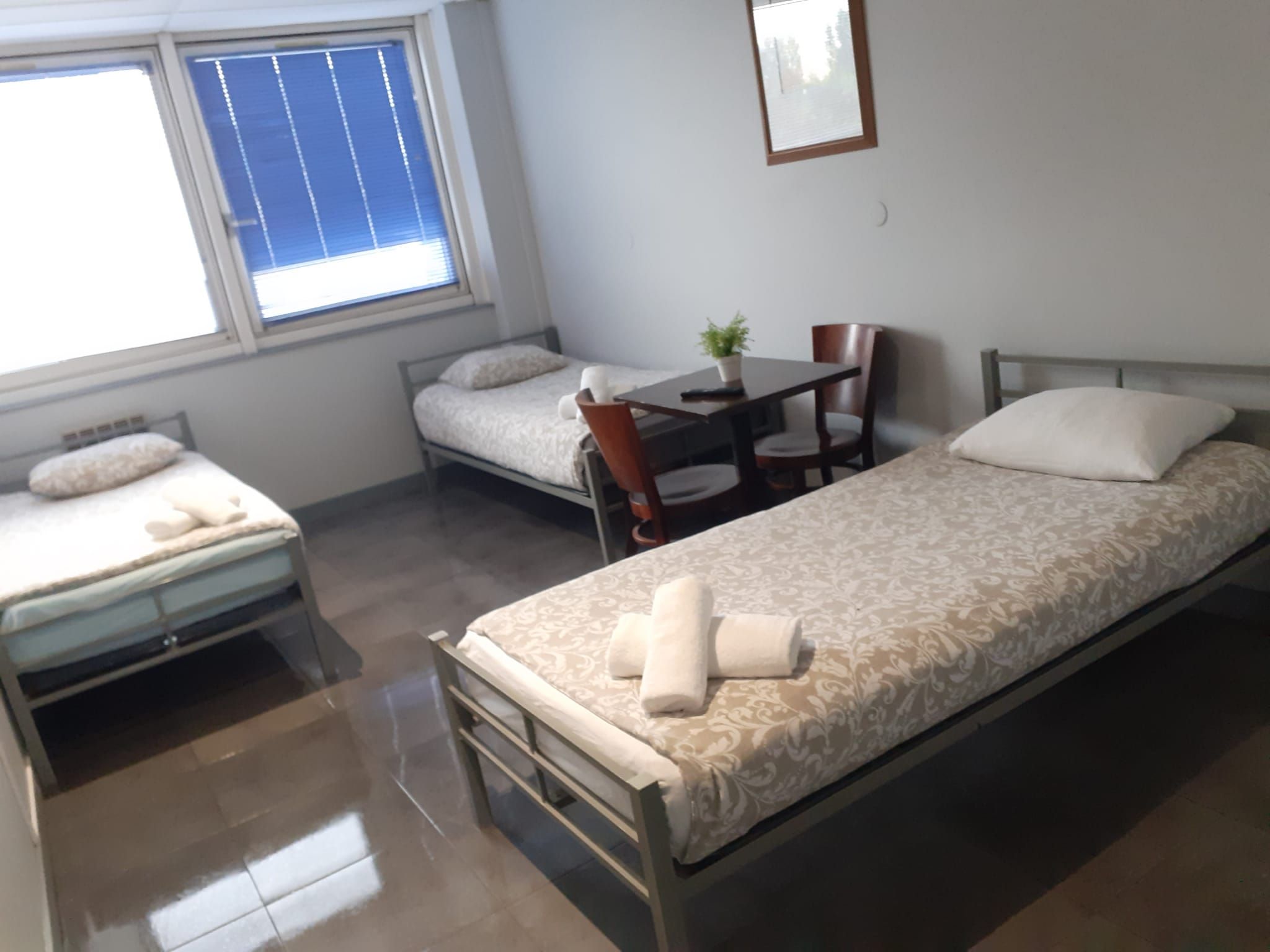 Una habitación pequeña y limpia con dos camas individuales, una mesa y una silla.