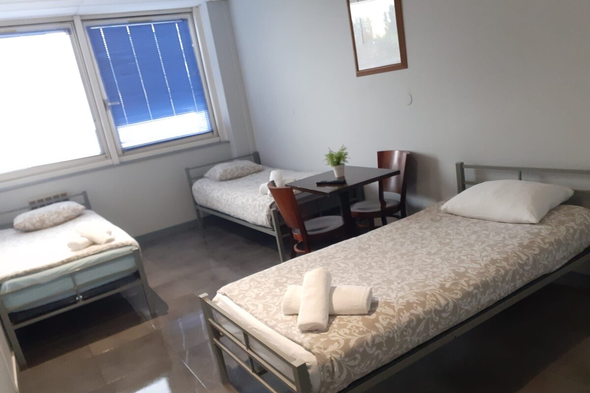 A small, clean room with two single beds, a table, and a chair.