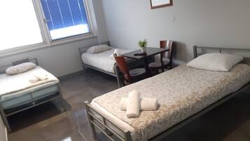 Una habitación pequeña y limpia con dos camas individuales, una mesa y una silla.