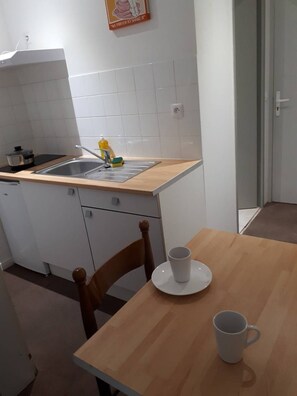 A small kitchen with a sink, a stove, and a table with two cups. - Appart Hotel (Champagne-sur-Oise)