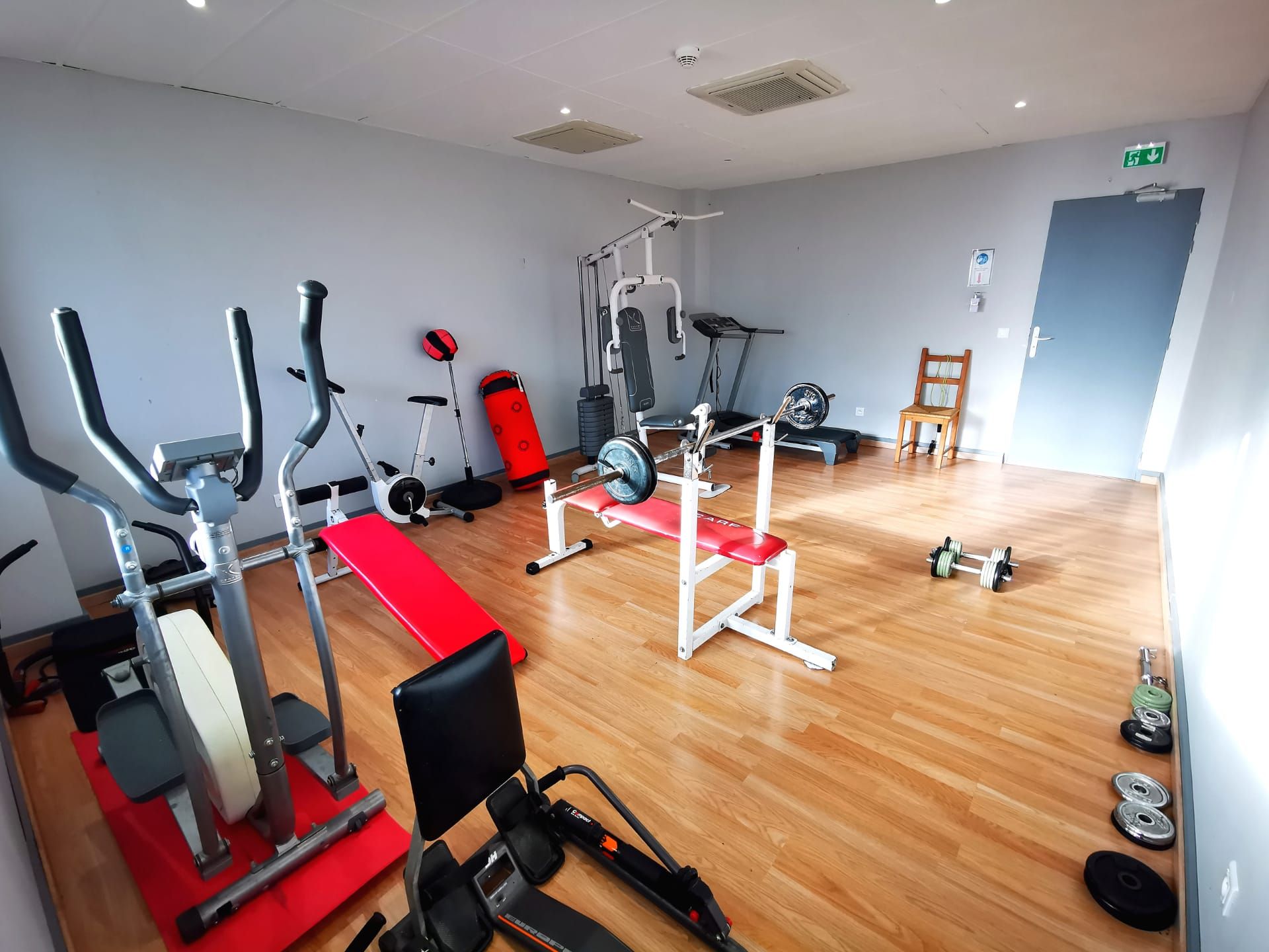A gym with cardio machines, weightlifting equipment, and a wooden floor.