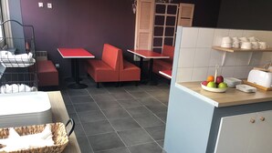 A restaurant with red seating, a counter with a fruit bowl, and a toaster. - Appart Hotel (Champagne-sur-Oise)