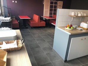A restaurant with red seating, a counter with a fruit bowl, and a toaster. - Appart Hotel (Champagne-sur-Oise)