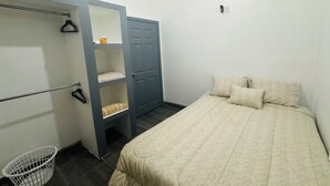 Un dormitorio con cama, armario, espejo, planta colgante y cesto de ropa.