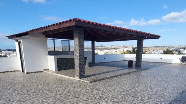 Un patio en la azotea con una zona de estar techada, piso de piedra y vistas de la ciudad.