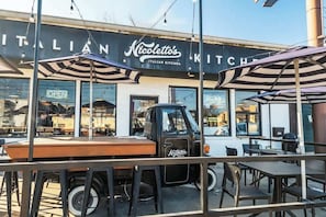 An outdoor seating area with tables and umbrellas in front of a building with a sign that reads "Nicolletto's Italian Kitchen."