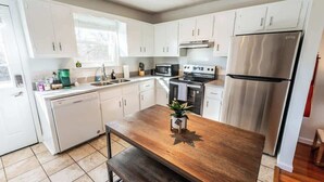 A modern kitchen with white cabinets, stainless steel appliances, and a wooden island. - The Eastside 2BR Near 5Points (Nashville)