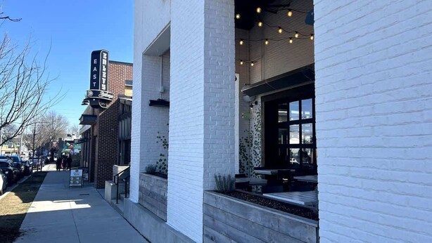 A building with a white brick facade, a sign indicating 'EAST' on the corner, and a visible entrance with outdoor seating. - The Eastside 2BR Near 5Points (Nashville)