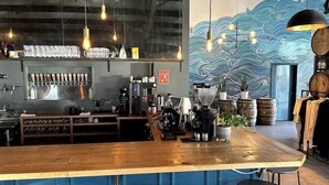 A bar area with a wooden counter, beer taps, and a coffee machine. There are hanging lights and a mural on the wall. - Riverside Retreat Near 5 Points (Nashville)