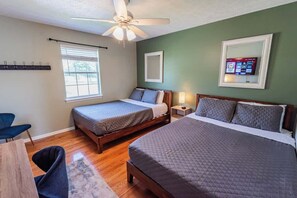 A bedroom with two beds, a ceiling fan, a window with blinds, a bedside table with a lamp, and a TV mounted on the wall. - Riverside Retreat Near 5 Points (Nashville)
