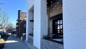 Un bâtiment à la façade en briques blanches, une enseigne indiquant « EST » au coin, et une entrée bien visible avec des places assises à l’extérieur.