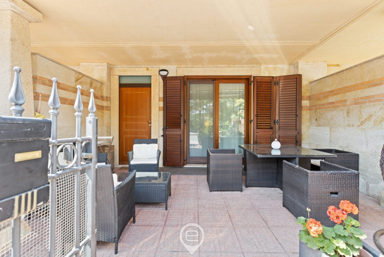 An outdoor patio area with wicker furniture, a glass table, and a potted plant.