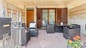 Ein Terrassenbereich im Freien mit Korbmöbeln, einem Glastisch und einem Blumentopf.