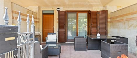 An outdoor patio area with wicker furniture, a glass table, and a potted plant.