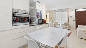 Eine moderne Küche mit integrierten Geräten, ein Essbereich mit Marmortisch und ein Wohnzimmer mit Sofa und Lampe.